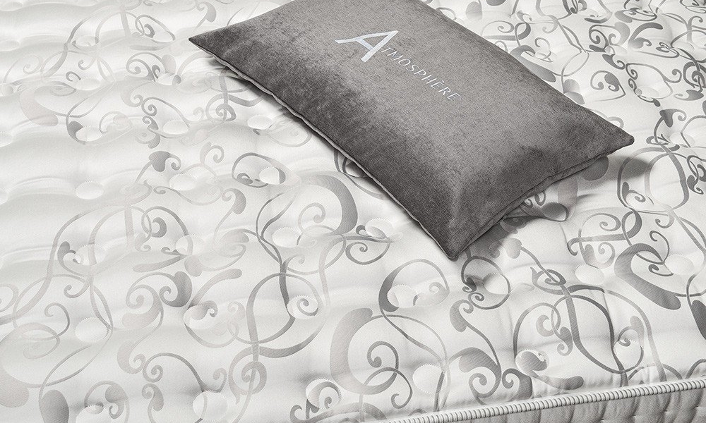 Un coussin décoratif avec le motif "ATMOSPHERE" repose gracieusement sur un matelas à motifs aux motifs tourbillonnants, évoquant l'élégance d'un canapé parisien. Son style vibrant évoque la qualité et le charme des intérieurs sophistiqués. Canape Paris by Atelier Bis