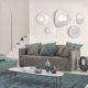 Découvrez un salon moderne doté d'un élégant canapé gris orné de coussins bleu sarcelle, de miroirs muraux abstraits et d'une table basse minimaliste, le tout faisant écho à la sophistication d'un showroom haut de gamme. Canape Paris by Atelier Bis