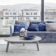 Découvrez un salon parisien moderne avec une table basse grise chic, des objets de décoration élégants et un canapé bleu moelleux. De grandes fenêtres offrent une vue imprenable sur le paysage urbain, alliant sophistication et charme chaleureux. Canape Paris by Atelier Bis