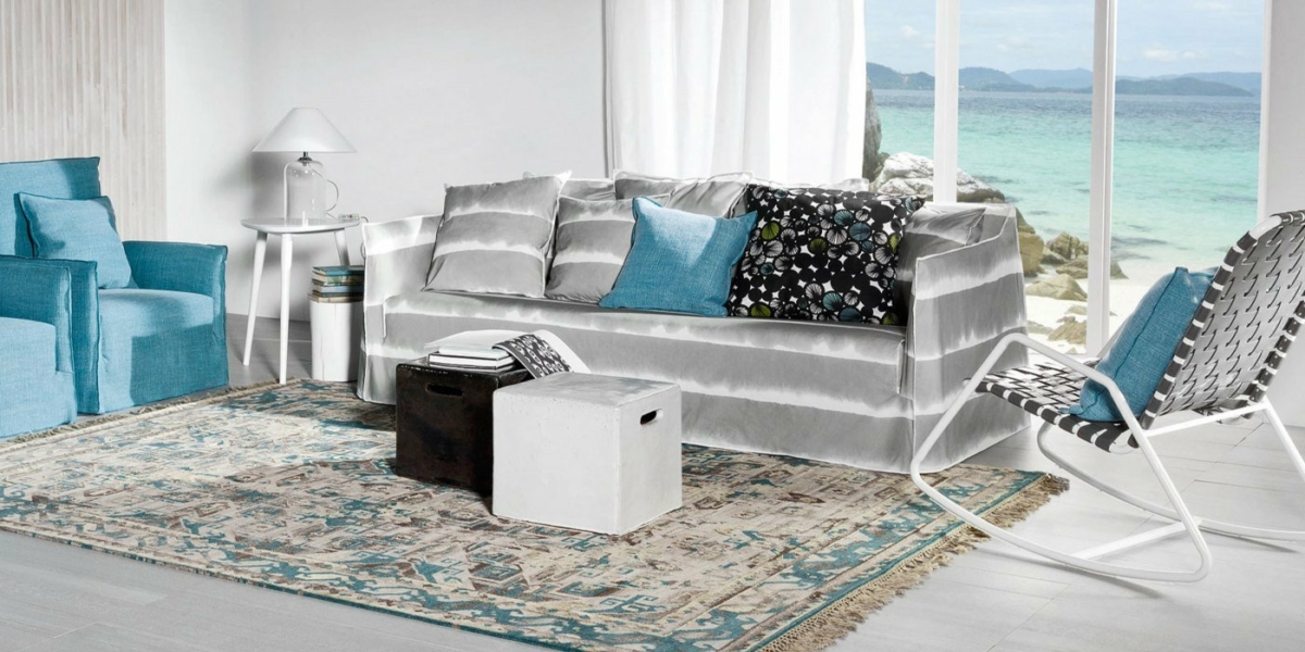 Entrez dans un salon côtier moderne qui canalise l'élégance d'un showroom parisien, avec un canapé rayé, des fauteuils bleus et un tapis à motifs avec une vue enchanteresse sur l'océan. Canape Paris by Atelier Bis