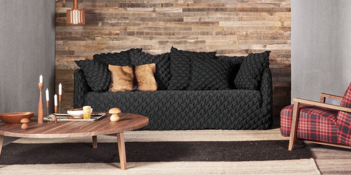 Salon cosy avec un canapé noir de haute qualité, une chaise à carreaux, une table basse en bois et un mur en bois rustique qui dégage une touche de charme parisien. Canape Paris by Atelier Bis