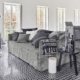 Salon moderne avec mobilier gris et coussins à motifs, rappelant un showroom parisien. Le sol carrelé complète un canapé confortable, tandis que le coin repas est élégamment installé sur une plate-forme surélevée. Canape Paris by Atelier Bis