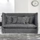 Un élégant canapé gris, orné de coussins à motifs noirs et blancs, orne cette pièce moderne rappelant un showroom parisien, avec une élégante horloge murale. Canape Paris by Atelier Bis