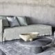 Salon moderne avec un canapé gris, des tables grises, un pouf tissé, un bol décoratif et un tapis texturé qui évoquent l'élégance chic d'un showroom parisien. Canape Paris by Atelier Bis