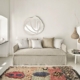 Chambre minimaliste avec un canapé beige, un miroir décoratif, des suspensions tissées et un tapis coloré au sol, apportant une touche d'élégance parisienne. Canape Paris by Atelier Bis