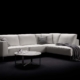 Canapé sectionnel blanc avec coussins et jeté gris, flanqué de tables rondes sur fond noir, reflétant l'élégance chic du décor parisien, où la qualité rencontre le style sans effort. Canape Paris by Atelier Bis