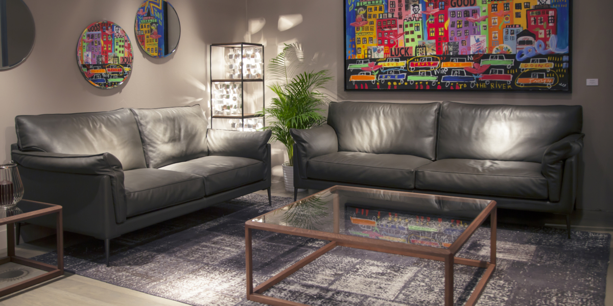 Un salon moderne comprend deux canapés en cuir noir, des œuvres d'art murales colorées, des miroirs ronds et une table basse en verre, où le style rencontre la qualité à un excellent prix. Canape Paris by Atelier Bis