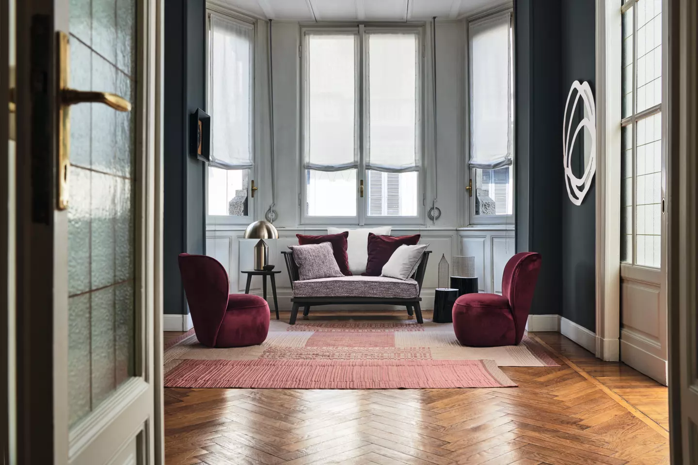 Salon moderne avec canapé, chaises en velours, tapis à motifs et grandes fenêtres avec rideaux transparents, offrant une ambiance de qualité et de style raffiné. Canape Paris by Atelier Bis