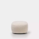 Un pouf doux, rond et beige clair orne un fond blanc uni, reflétant la qualité sans effort que l'on trouve généralement dans un showroom parisien. Canape Paris by Atelier Bis
