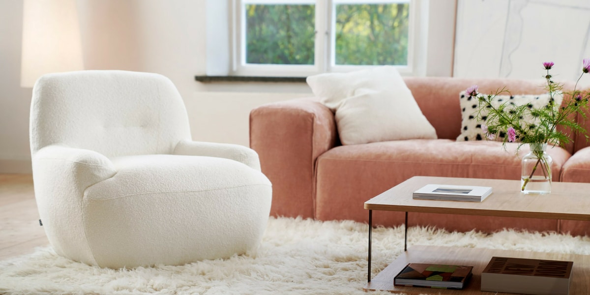 Fauteuil Uma en velours blanc avec un tapis marron et des accents jaunes Le fauteuil en velours blanc repose sur un tapis marron, avec des accents jaunes dispersés dans la pièce pour une touche de gaieté.