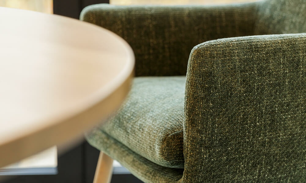Fauteuil Moa Bistro en cuir brun dans un salon avec des murs en briques apparentes Le fauteuil en cuir brun se trouve dans un salon industriel avec des murs en briques apparentes, créant une ambiance chaleureuse et rustique.