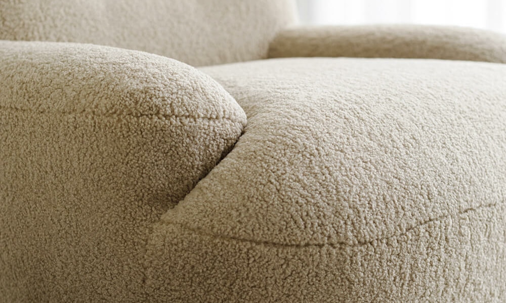 Fauteuil Uma en tissu marron avec des rideaux blancs et jaunes Le fauteuil en tissu marron est placé près de rideaux blancs et jaunes, apportant une touche harmonieuse à la décoration du salon.
