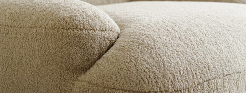 Fauteuil Uma en tissu marron avec des rideaux blancs et jaunes Le fauteuil en tissu marron est placé près de rideaux blancs et jaunes, apportant une touche harmonieuse à la décoration du salon.