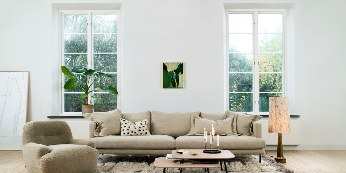 Fauteuil Uma en tissu blanc avec une table d'appoint en bois et une lampe jaune Le fauteuil en tissu blanc est accompagné d'une table d'appoint en bois et d'une lampe jaune, créant une ambiance chaleureuse et accueillante.
