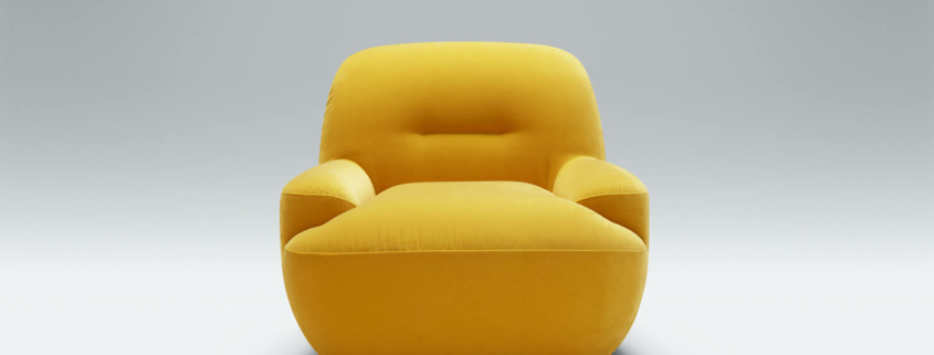 Fauteuil Uma en tissu jaune moutarde avec des coussins marron Le fauteuil en tissu jaune moutarde est agrémenté de coussins marron, apportant une touche chaleureuse et accueillante au salon.