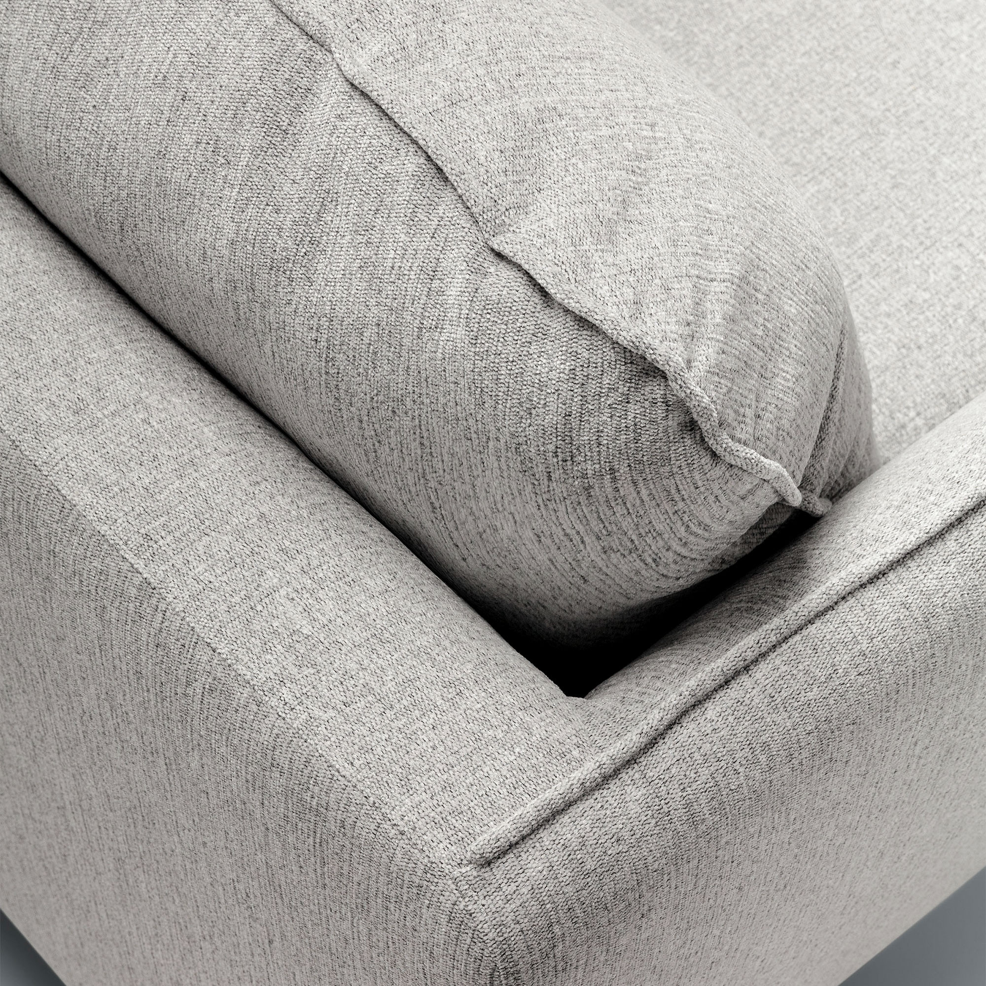Gros plan d'un canapé gris rembourré dans une salle d'exposition, avec un tissu texturé et un coussin moelleux sur l'accoudoir. Canape Paris by Atelier Bis