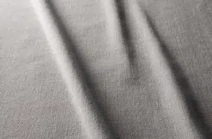 Tissu gris clair avec une surface texturée et des plis doux et diagonaux créant des ombres légères. Canape Paris by Atelier Bis
