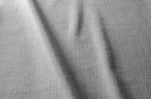 Tissu texturé gris avec des plis visibles et des ombres subtiles traversant la surface en diagonale. Canape Paris by Atelier Bis