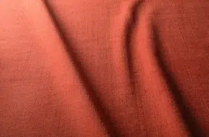 Gros plan sur un tissu souple, rouge-orange, aux plis délicats et à la surface texturée. Canape Paris by Atelier Bis