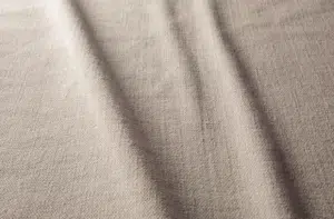 Tissu beige texturé avec de légers plis créant des ombres douces sur la surface. Canape Paris by Atelier Bis