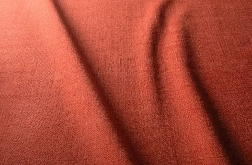 Gros plan d'un tissu texturé brun rougeâtre avec des plis et des ombres doux et diagonaux. Canape Paris by Atelier Bis