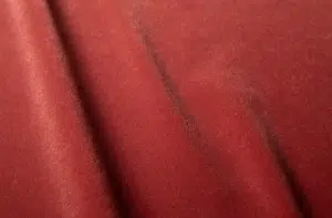 Gros plan sur un tissu de velours rouge à la texture douce et aux plis diagonaux subtils. Canape Paris by Atelier Bis