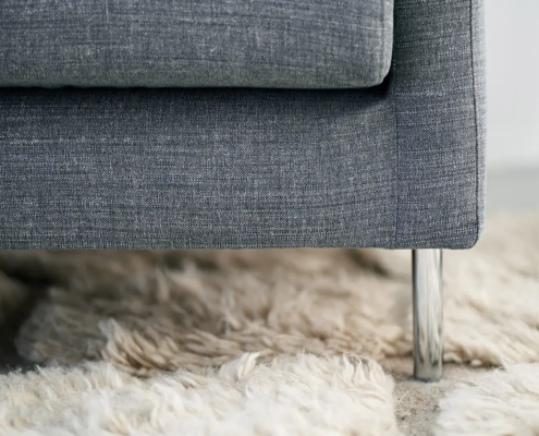 Gros plan d'un canapé gris avec des pieds en métal sur un tapis beige moelleux. Canape Paris by Atelier Bis