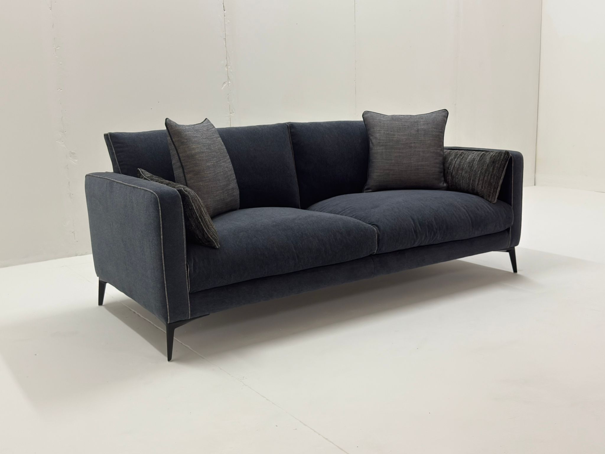 Canapé moderne gris foncé avec quatre coussins dans une pièce blanche minimaliste. Canape Paris by Atelier Bis
