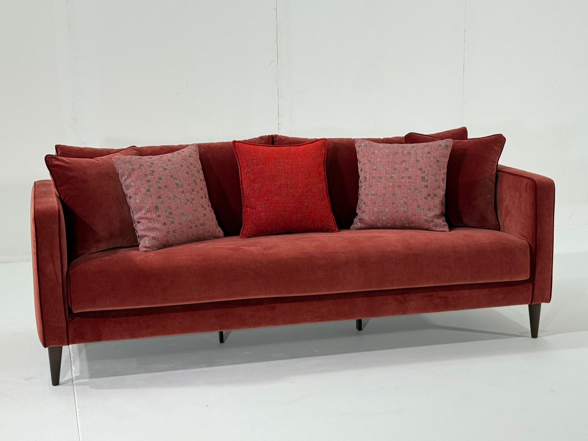 Canapé en velours rouge avec cinq coussins assortis, disposés sur un fond blanc uni. Canape Paris by Atelier Bis