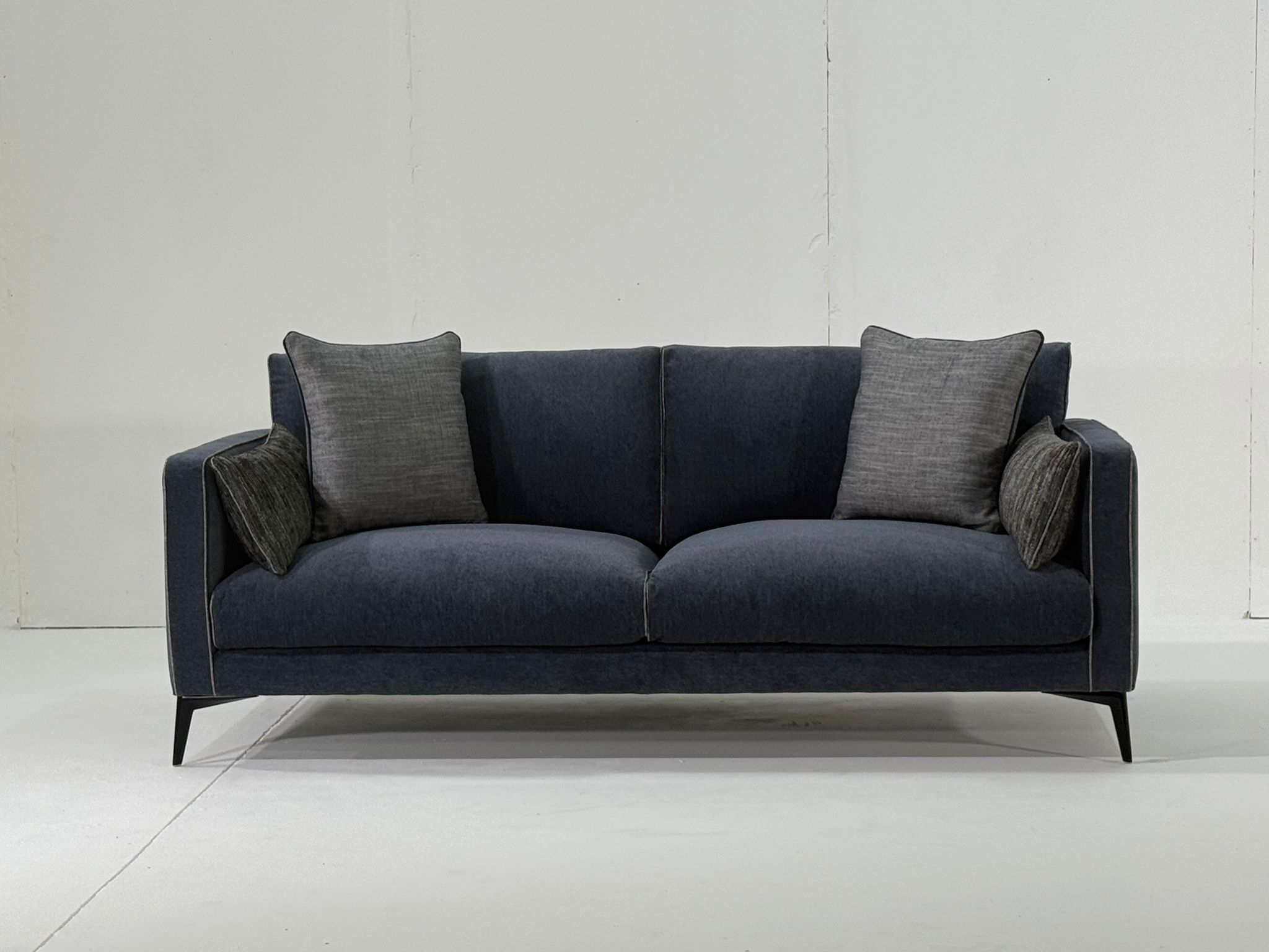 Un canapé moderne bleu foncé avec quatre coussins gris, sur un fond blanc uni. Canape Paris by Atelier Bis