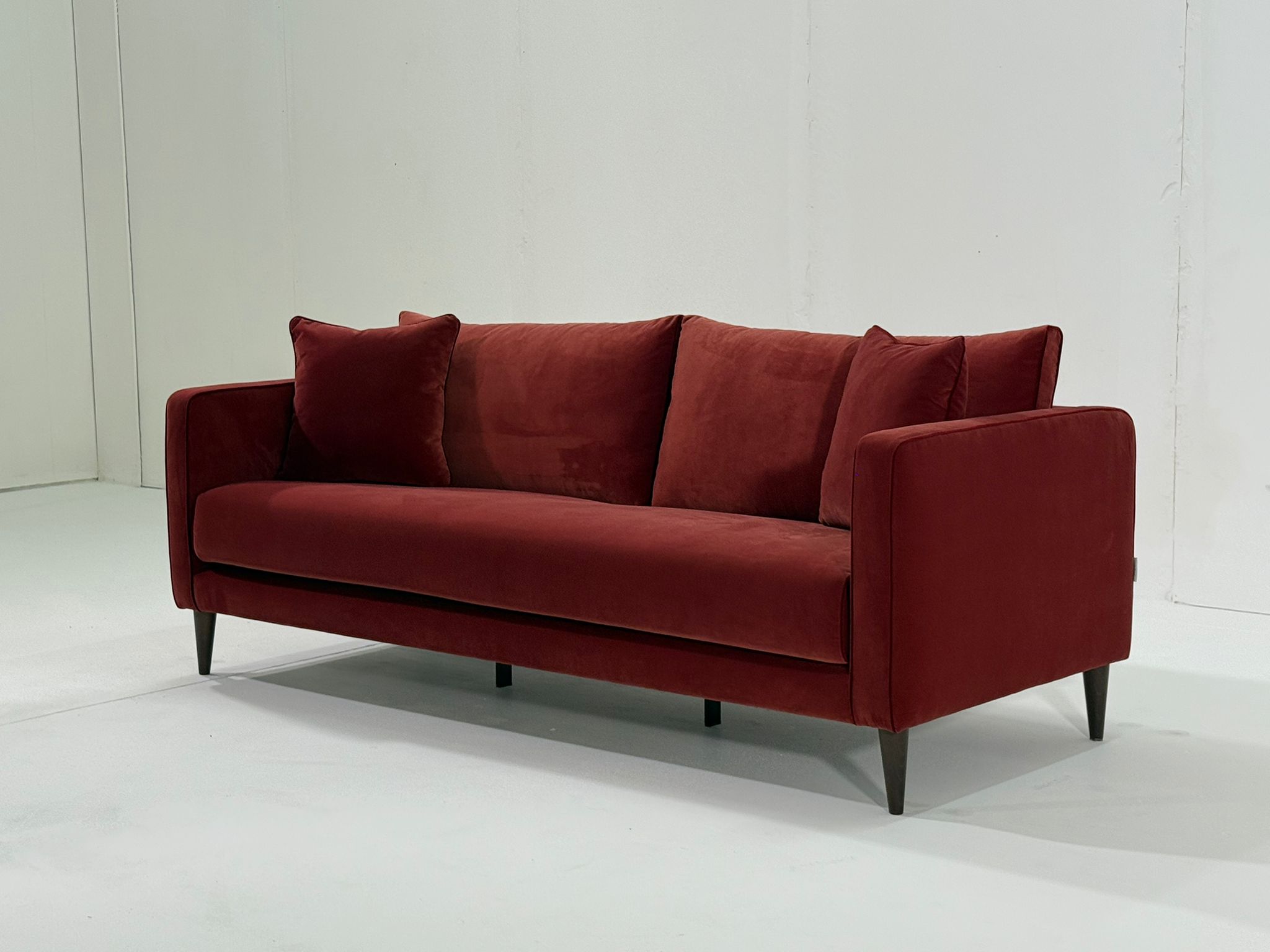 Un canapé moderne en velours rouge avec deux coussins, posé sur un fond blanc uni. Canape Paris by Atelier Bis