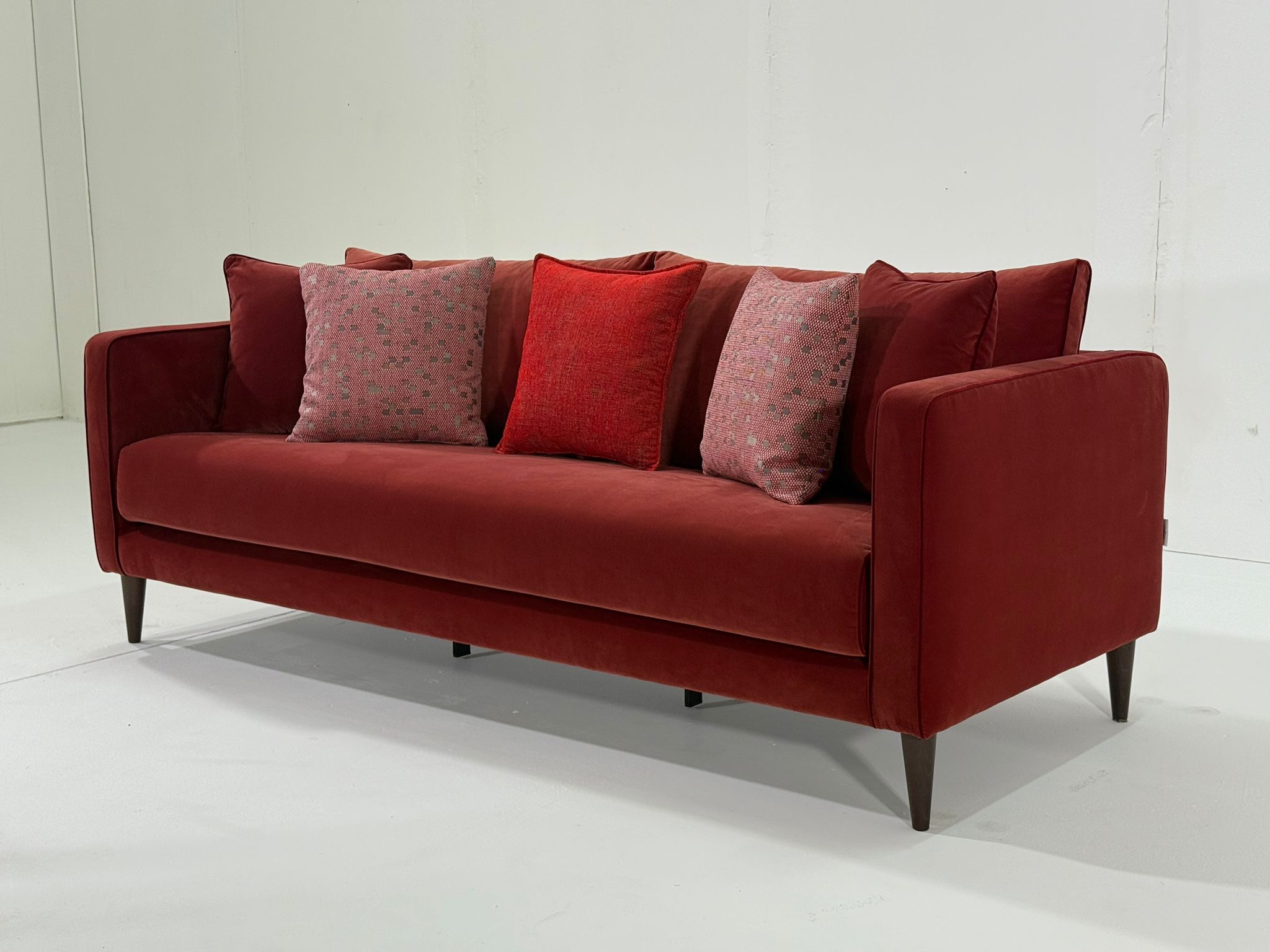 Un canapé rouge moderne avec quatre coussins à motifs sur fond blanc. Canape Paris by Atelier Bis