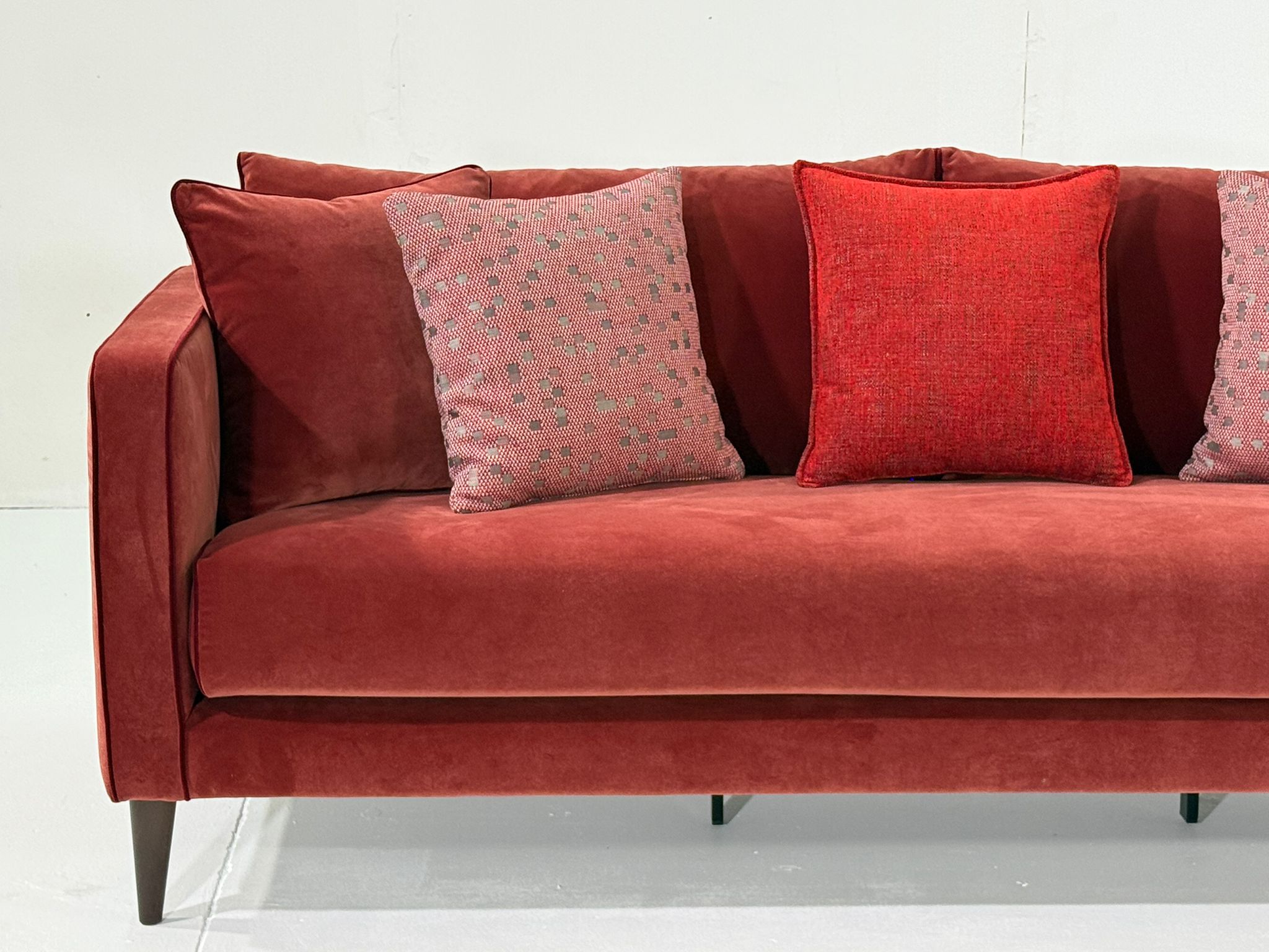 Canapé en velours rouge avec trois coussins décoratifs, disposés sur un fond blanc uni. Canape Paris by Atelier Bis