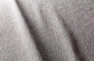 Gros plan d'un tissu gris texturé avec des lignes verticales visibles et des plis souples créant des zones d'ombre. Canape Paris by Atelier Bis