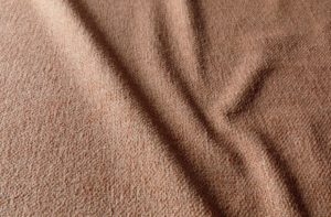 Gros plan d'un tissu texturé, brunâtre, avec des plis visibles et des ombres douces. Canape Paris by Atelier Bis