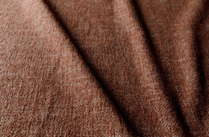 Gros plan sur un tissu brun texturé dont la trame est visible et dont les plis légers créent des motifs d'ombre. Canape Paris by Atelier Bis