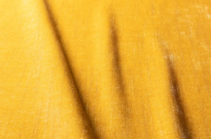 Gros plan sur un tissu jaune dont la texture est visible et dont les ombres créent des lignes diagonales sur la surface. Canape Paris by Atelier Bis