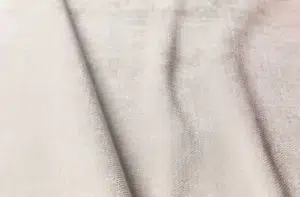 Gros plan d'un tissu beige clair à la texture subtile et aux plis doux qui s'étendent en diagonale sur la surface. Canape Paris by Atelier Bis