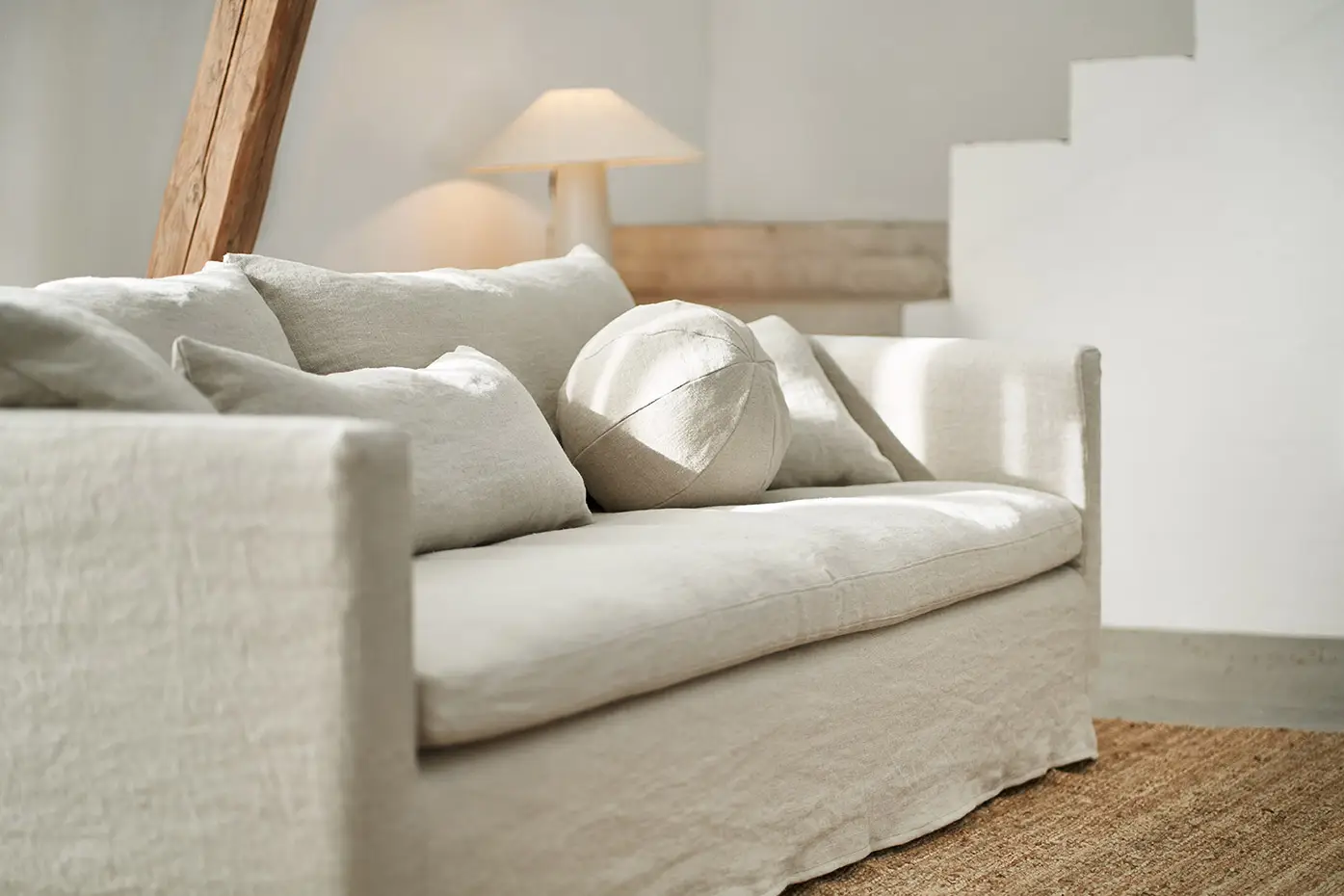 Canapé crème avec des coussins neutres dans un salon lumineux et minimaliste avec une lampe et un tapis. Canape Paris by Atelier Bis