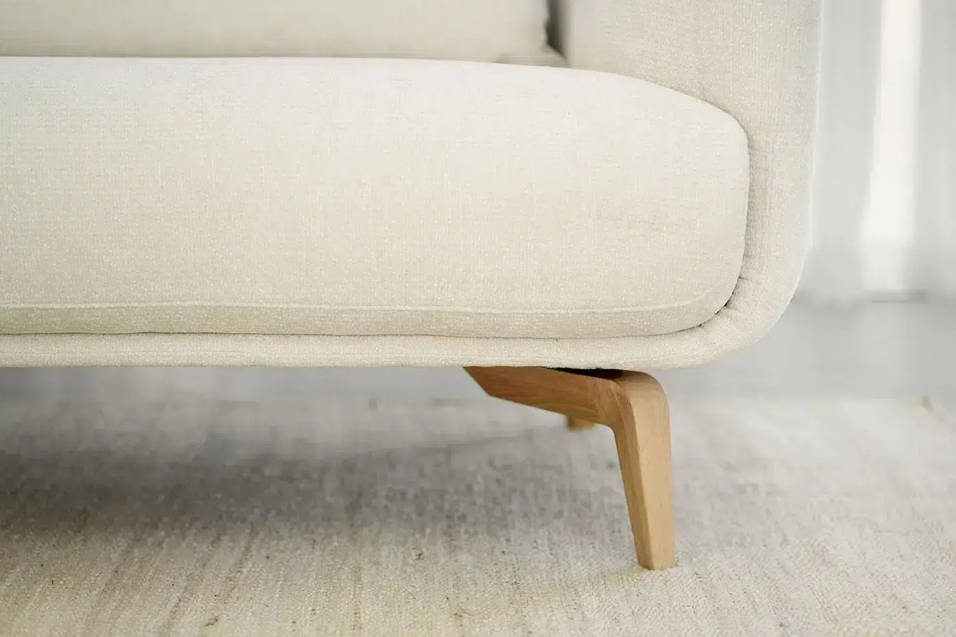 Gros plan sur un canapé beige rembourré avec des pieds en bois sur un tapis de couleur claire. Canape Paris by Atelier Bis