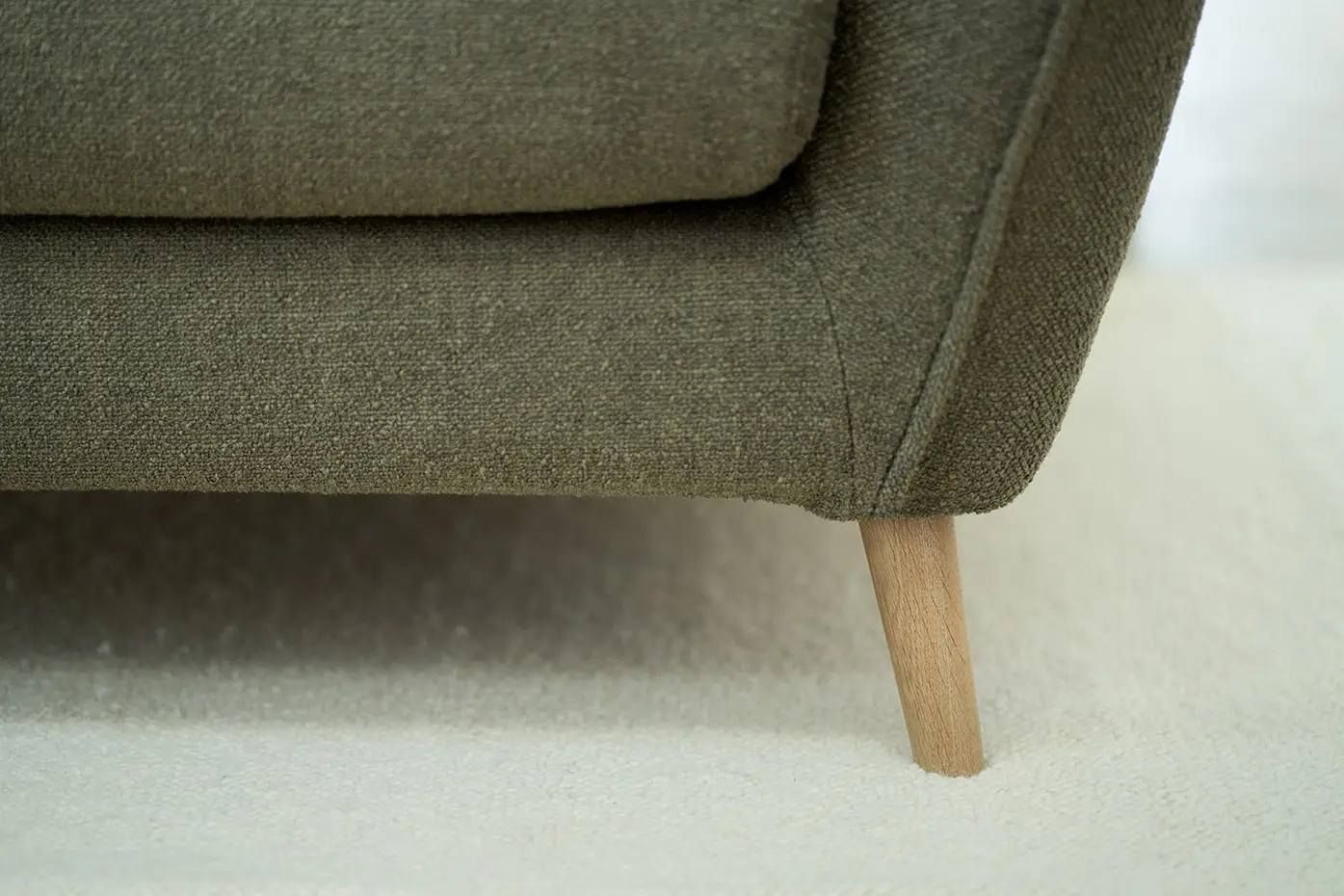 Gros plan sur un canapé en tissu vert avec des pieds en bois sur une moquette blanche. Canape Paris by Atelier Bis