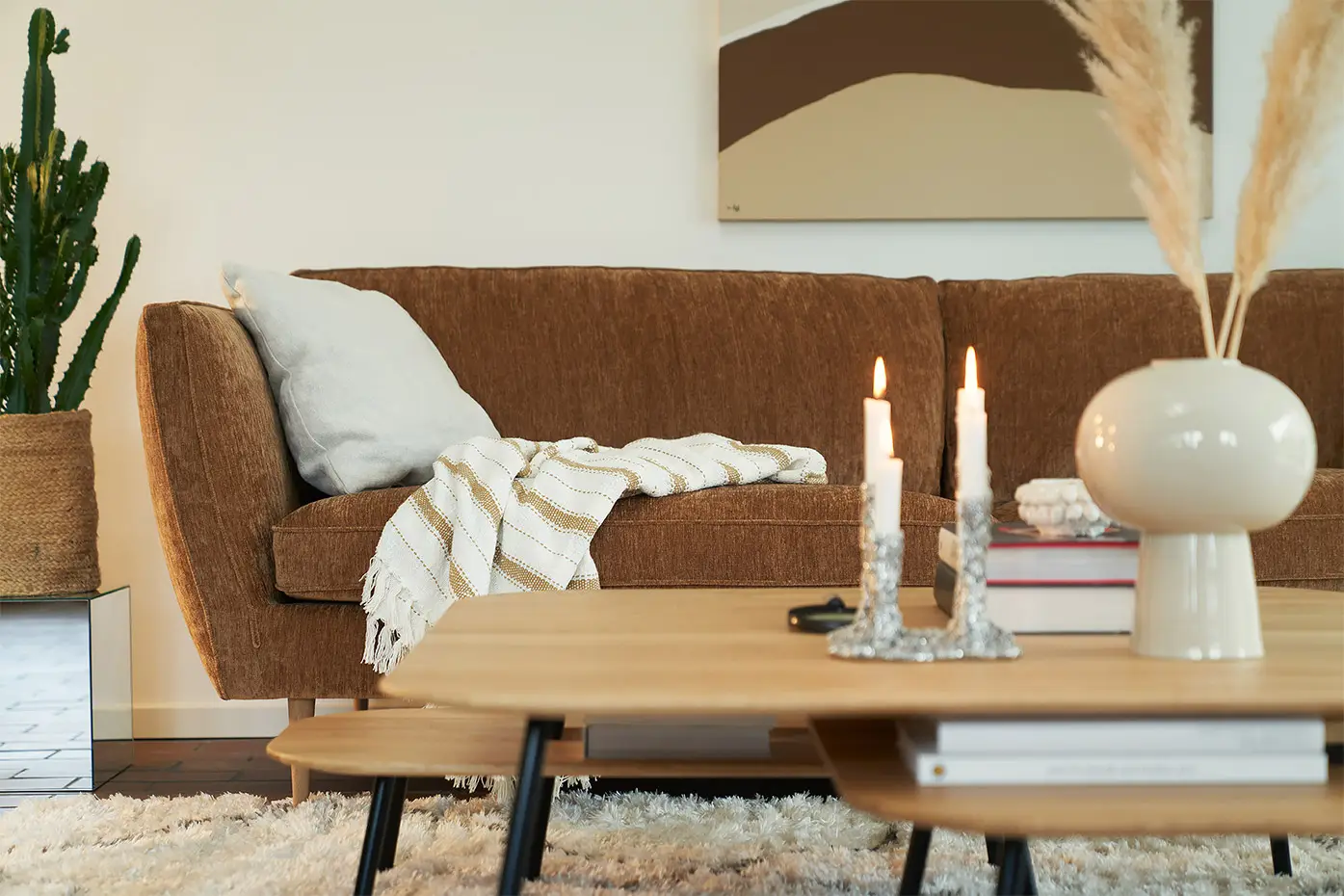 Canapé marron avec une couverture rayée, table basse avec des bougies et un cactus en pot dans un salon confortable. Canape Paris by Atelier Bis