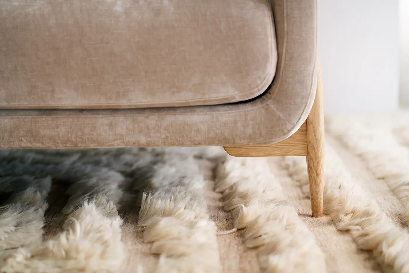 Gros plan sur un pied de canapé beige posé sur un tapis moelleux de couleur crème. Canape Paris by Atelier Bis