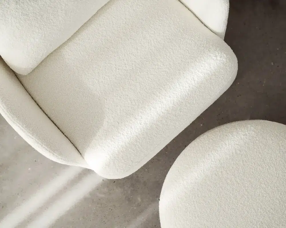 Gros plan d'un fauteuil crème texturé et d'un ottoman rond sur un sol en béton gris éclairé par la lumière du soleil. Canape Paris by Atelier Bis