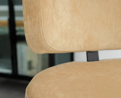 Gros plan d'une chaise beige rembourrée sur fond flou d'étagères. Canape Paris by Atelier Bis