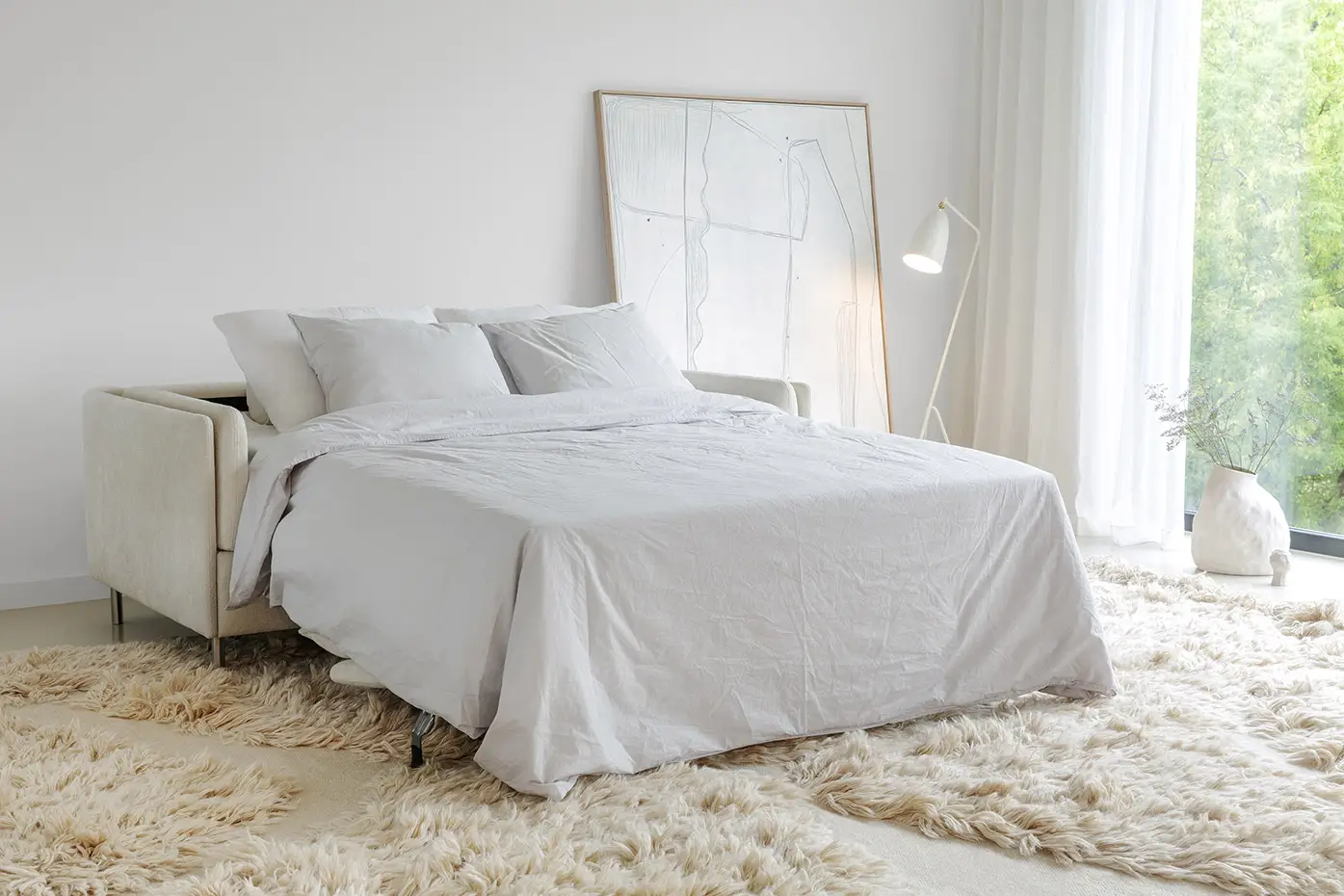 Chambre à coucher lumineuse avec un canapé-lit blanc, un tapis moelleux, un lampadaire et des œuvres d'art abstraites contre le mur. Canape Paris by Atelier Bis