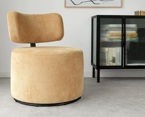 Un fauteuil pivotant moderne de couleur beige est posé sur un sol gris à côté d'un meuble en verre noir dans une pièce minimaliste. Canape Paris by Atelier Bis