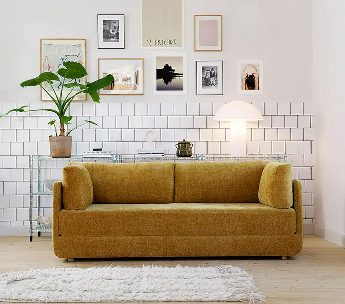 Canapé jaune moutarde dans un salon moderne avec art mural, plante d'intérieur, lampe et tapis blanc sur sol en bois. Canape Paris by Atelier Bis